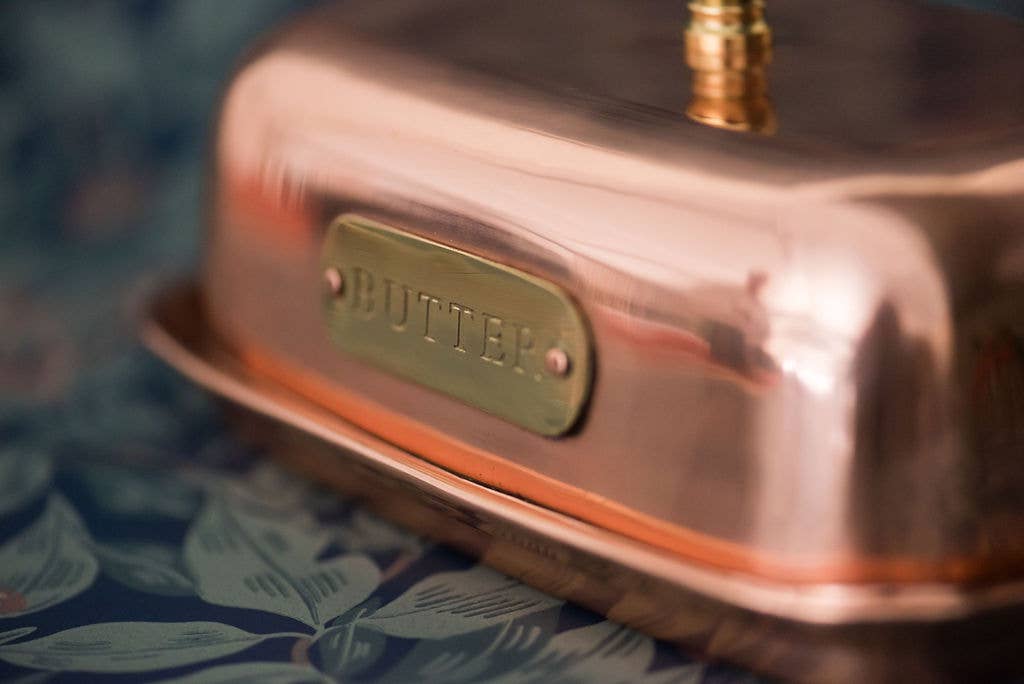 Copper butter container with a 'Butter' label on a floral-patterned surface