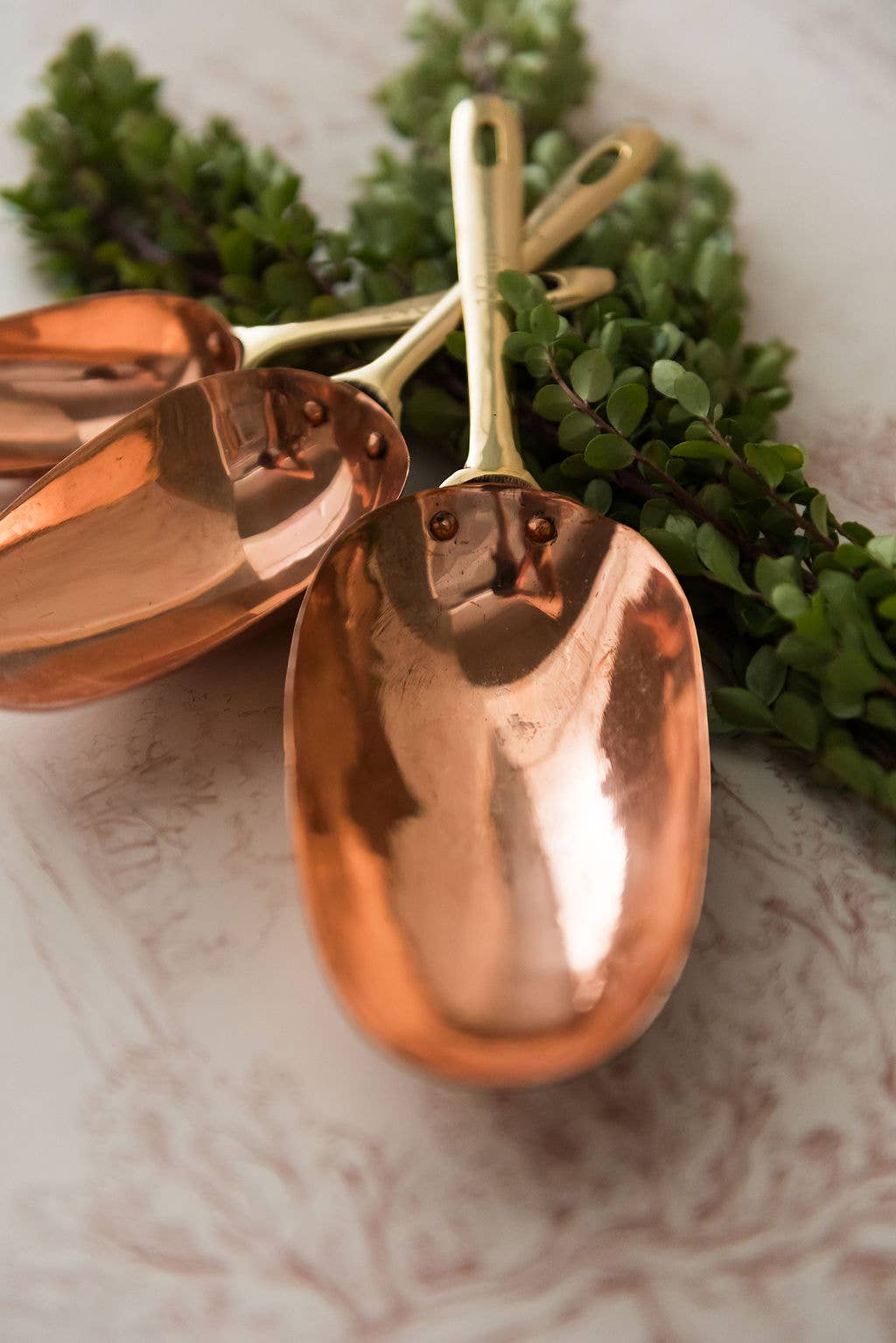 Set of copper measuring spoons on a marble surface with greenery in the background
