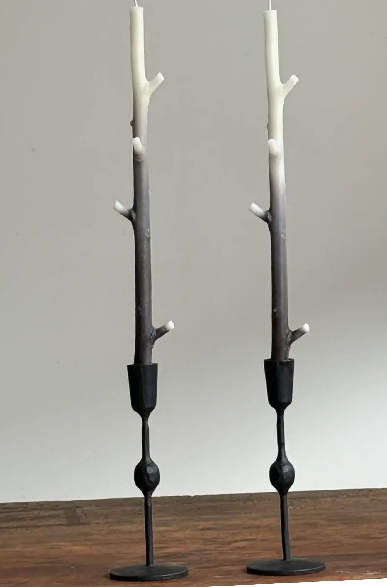 Two black candle holders with branch-like ombre black to white candles on a wooden surface.