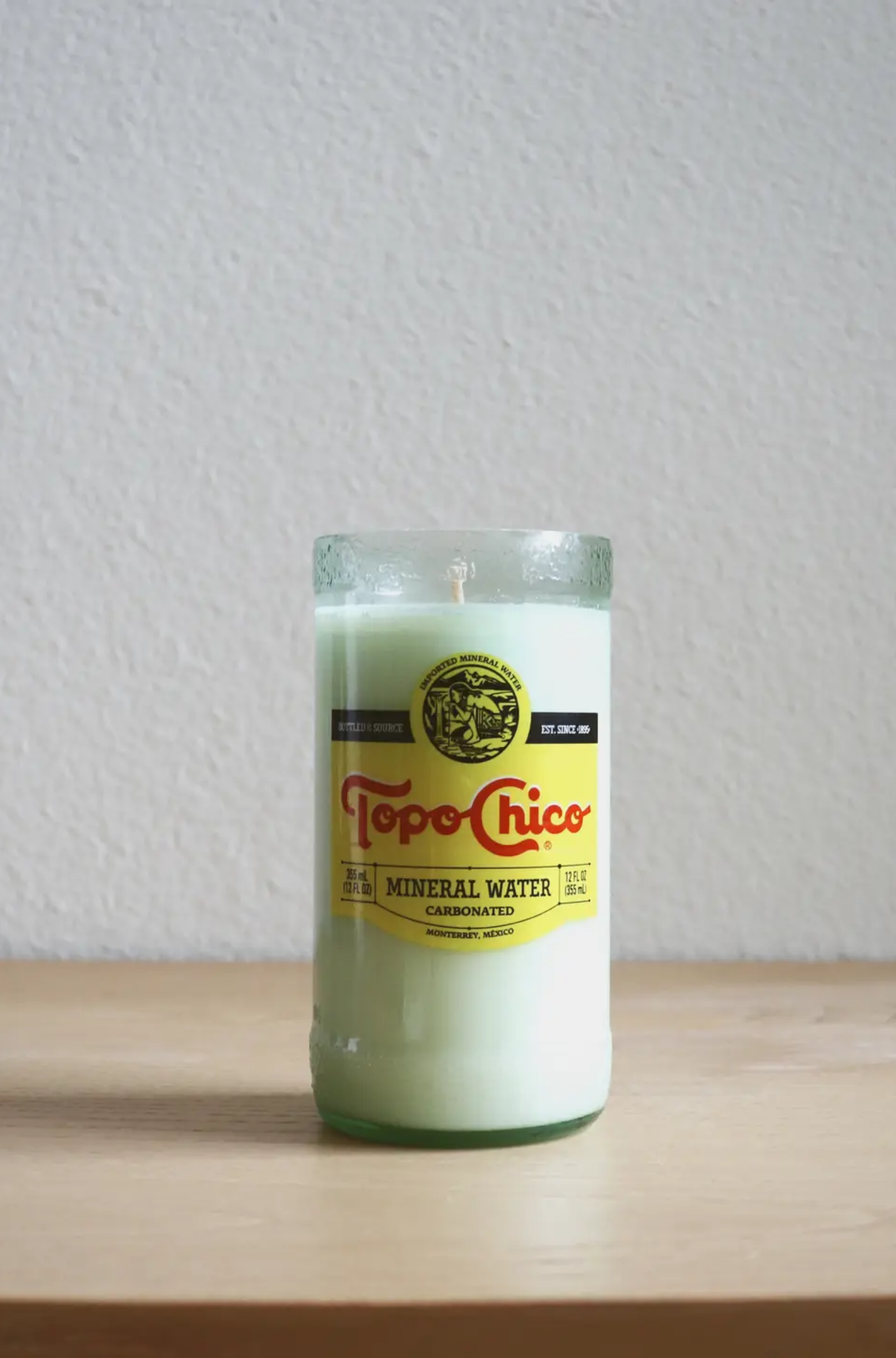 Topo Chico bottle repurposed as a candle with label still attached on a wooden surface.