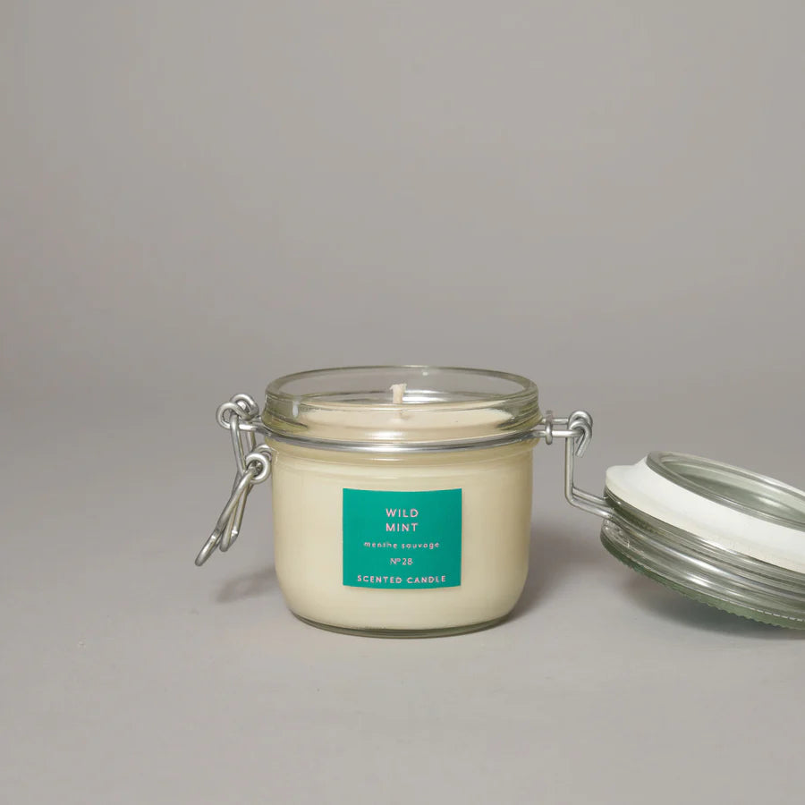 A medium-sized clear glass jar with a clip top lid containing a wild mint candle, labeled with the brand True Grace.