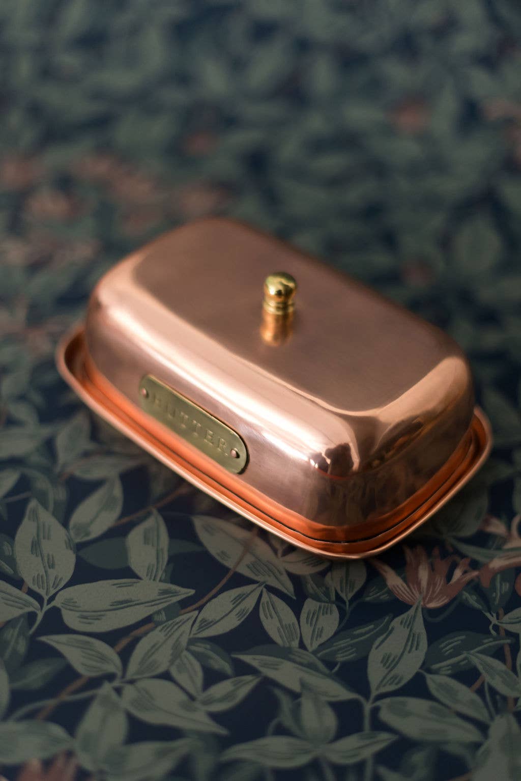 Copper-colored butter dish with a gold accent on a floral-patterned surface