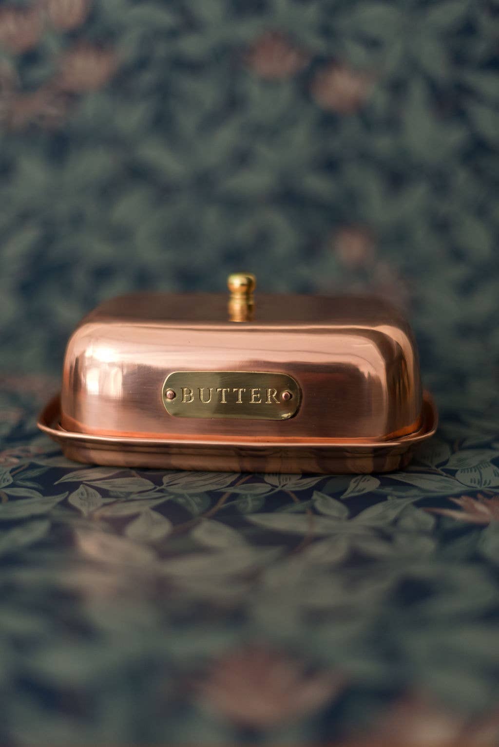Copper butter dish with a lid on a textured green surface