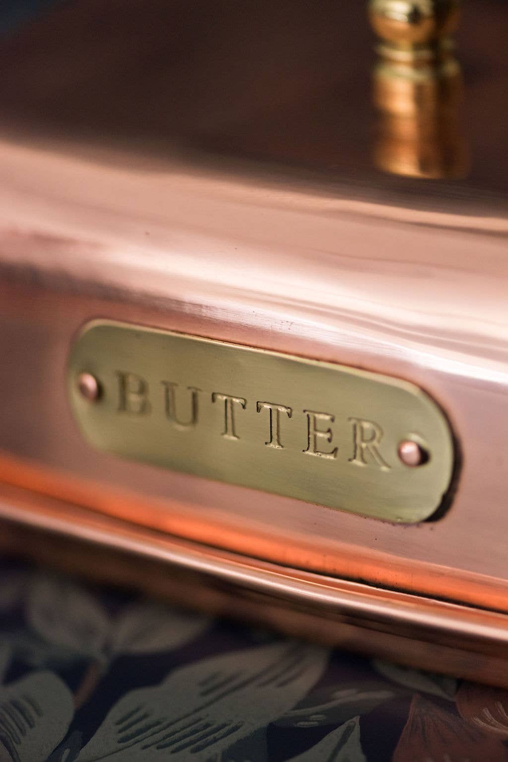 Copper butter churn with a brass label reading 'BUTTER' on a floral background.