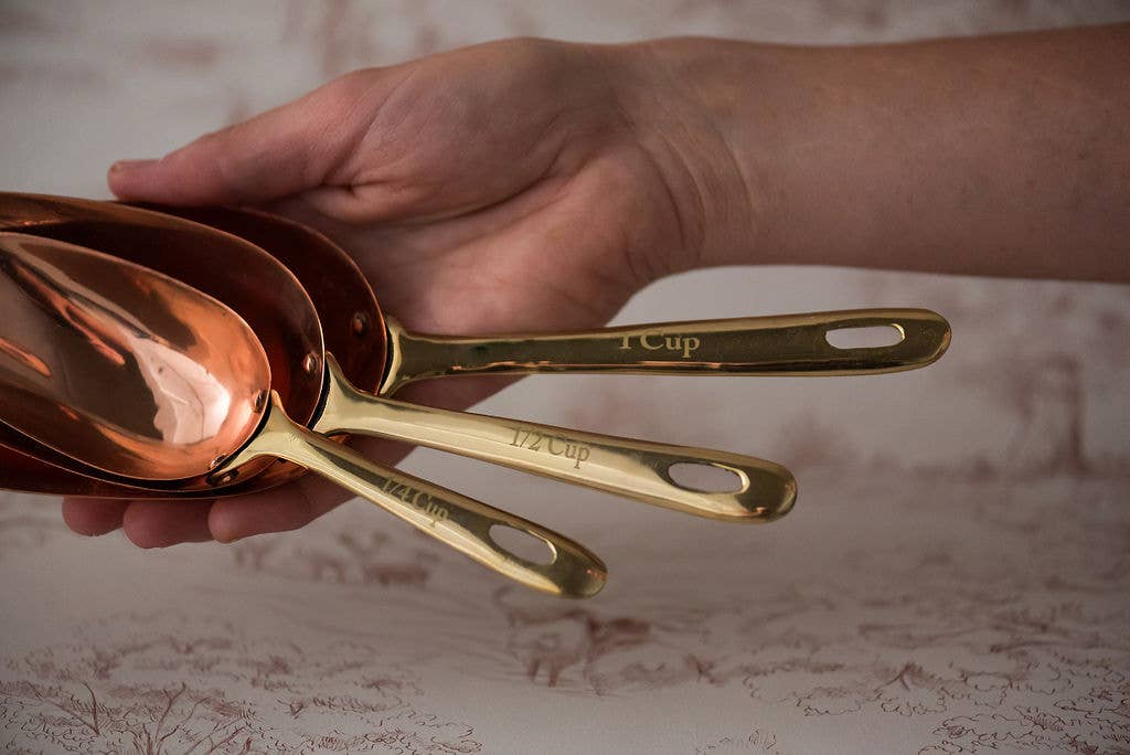 Set of gold measuring spoons held by a hand on a textured surface