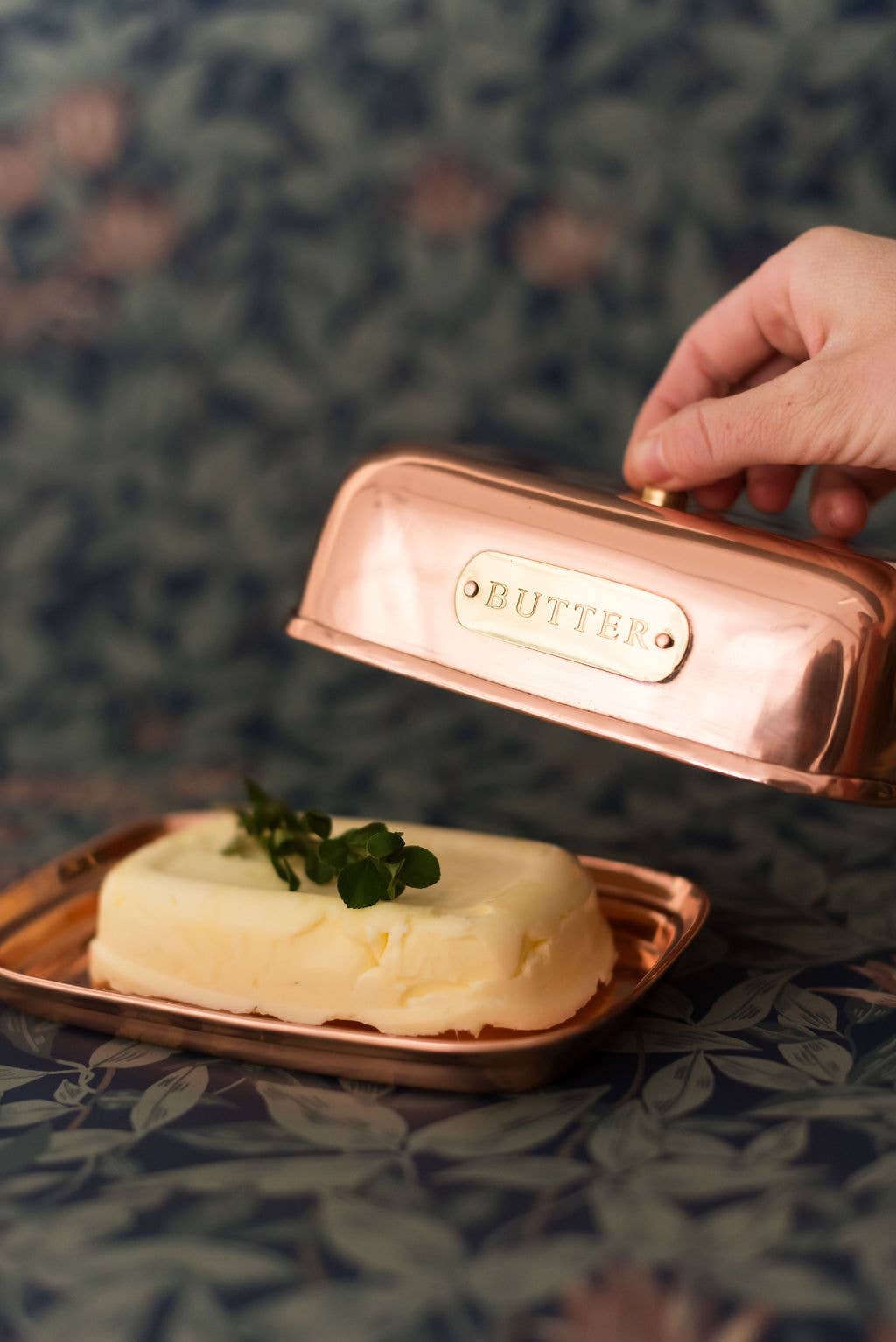 Copper butter dish with a pat of butter on a floral tablecloth
