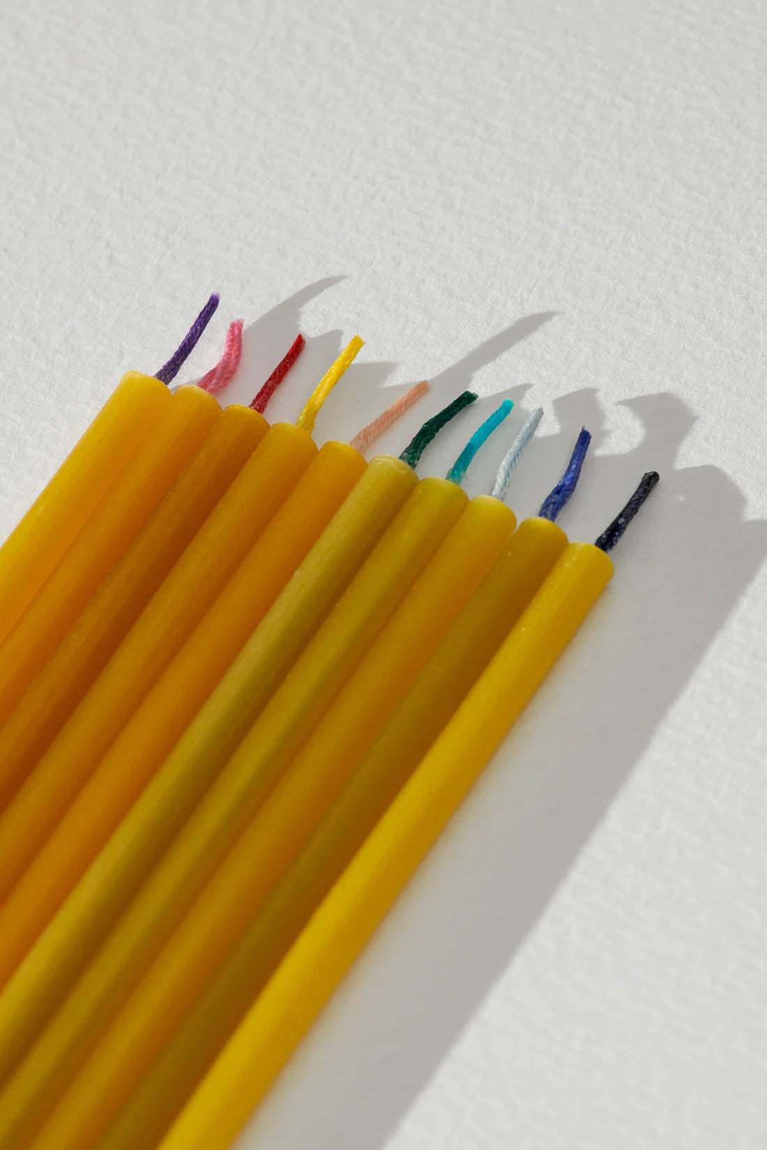 Yellow beeswax birthday candles with colorful wicks on a white background