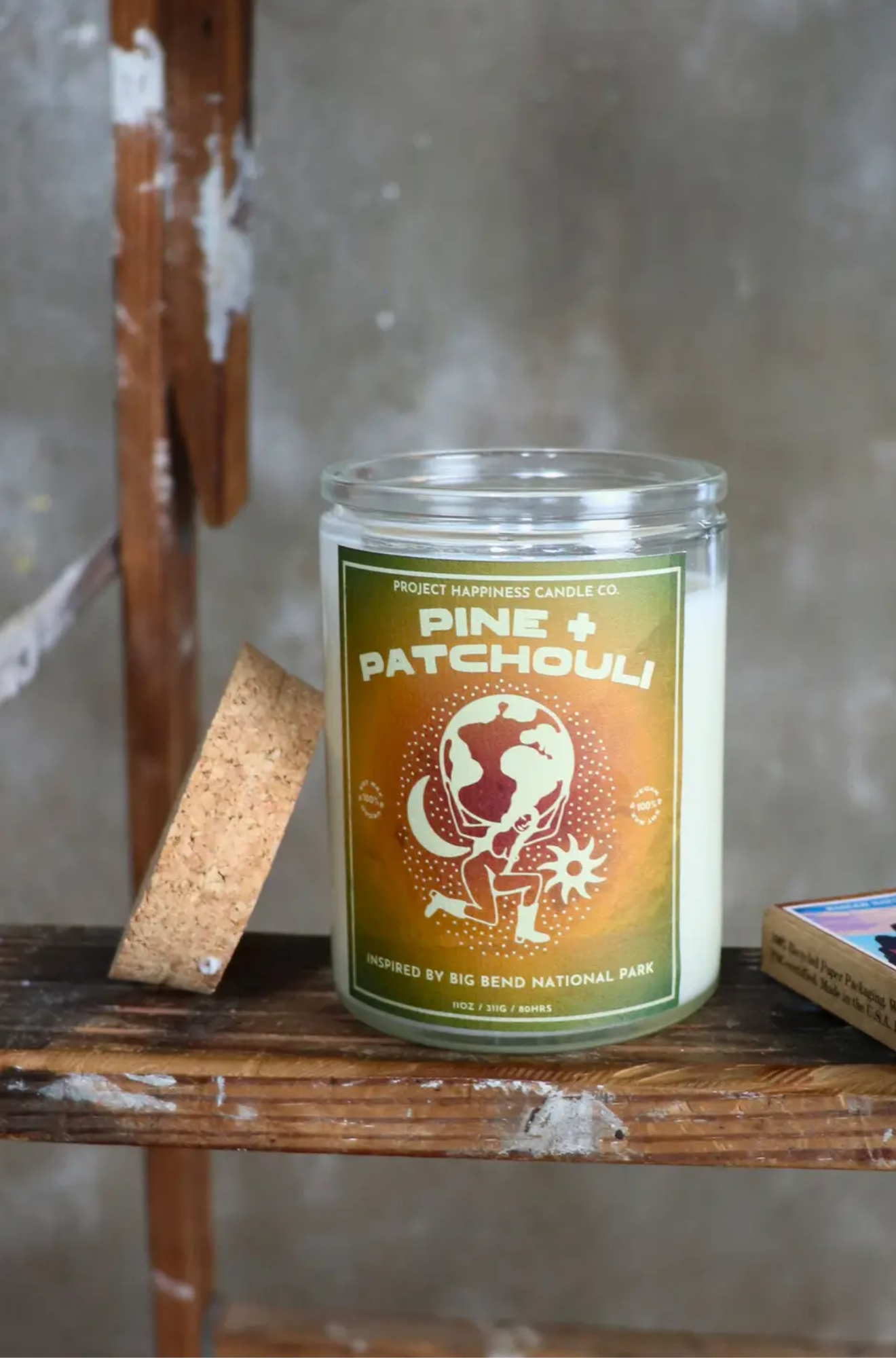 Candle labeled 'Pine + Patchouli' on a wooden surface with a rustic background