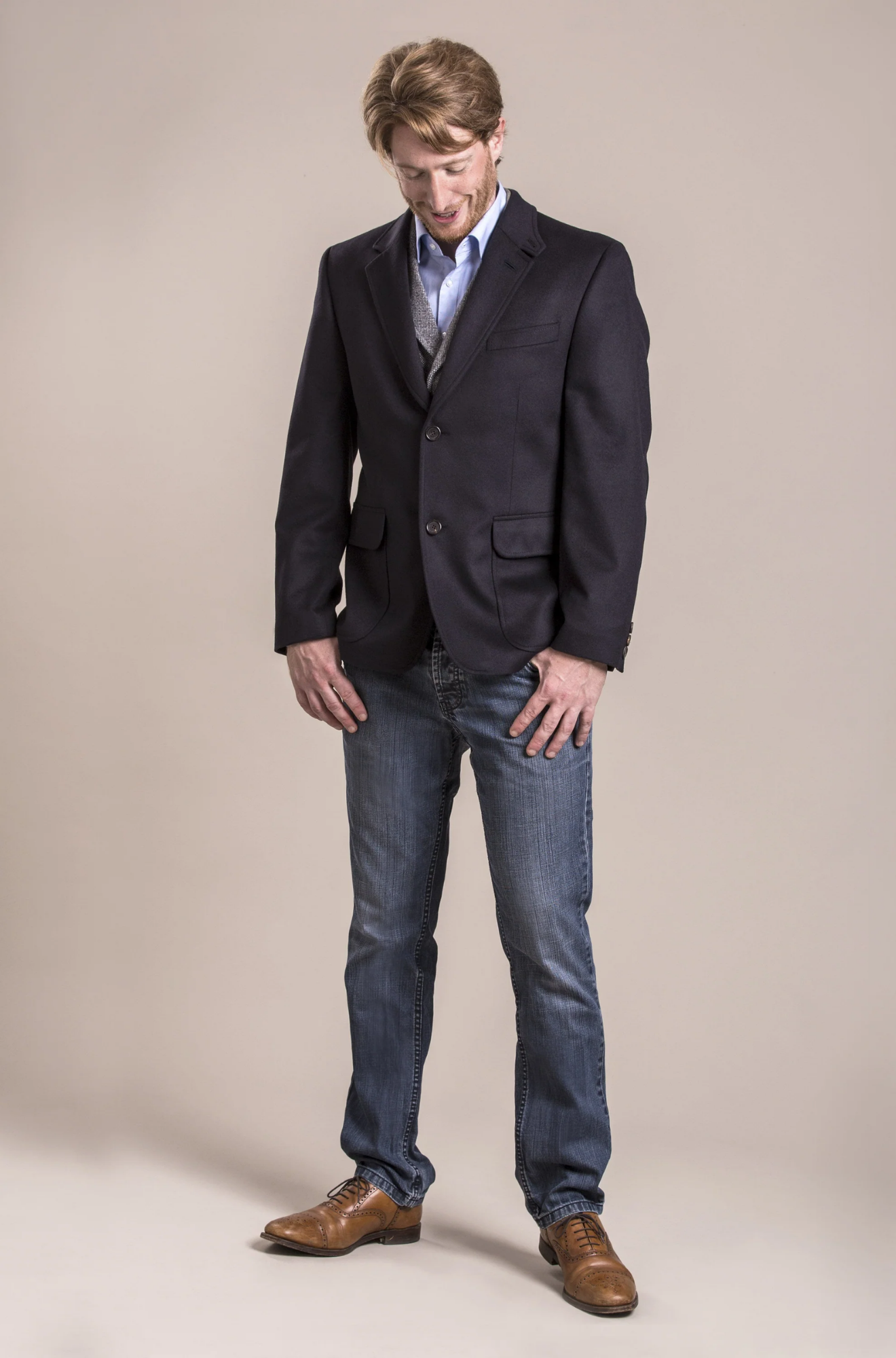 Man wearing a dark blazer, light shirt, and jeans on a beige background